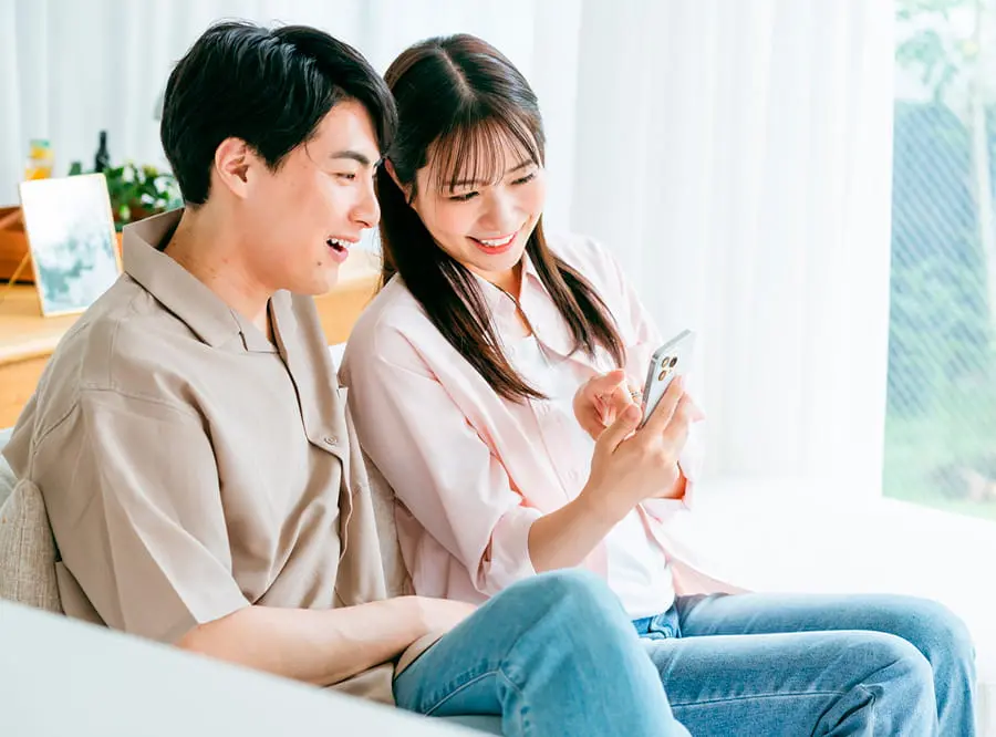 ソファに座った若い男女がスマートフォンの画面を一緒に見て楽しんでいる様子