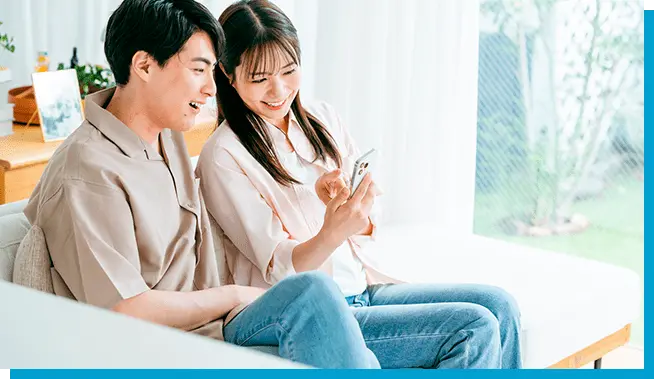 ソファに座った若い男女がスマートフォンの画面を一緒に見て楽しんでいる様子
